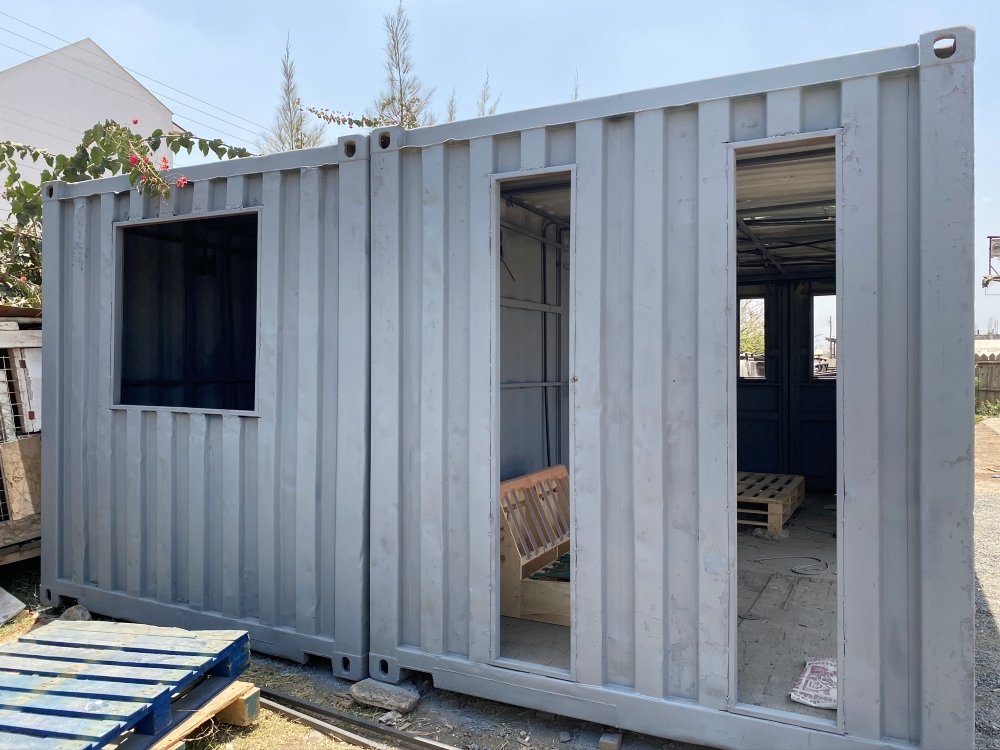 Shipping container during early construction stage with window and door openings cut out, photographed at a fabrication yard in Kenya.